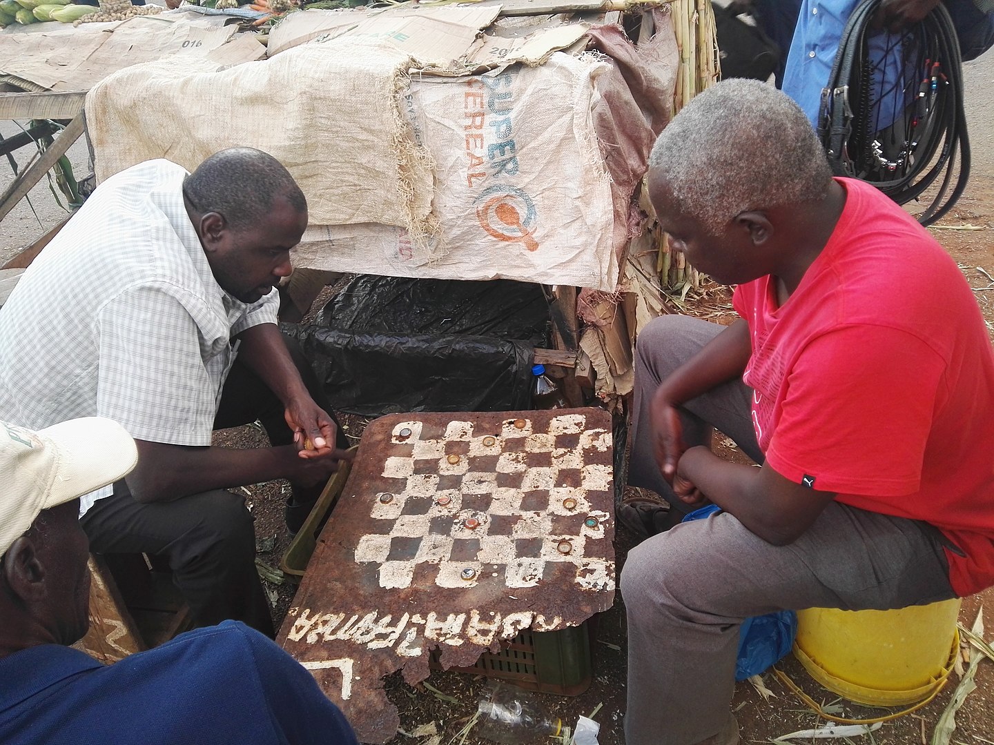 Fotografía que muestra dos hombres africanos jugando ajedrez en condiciones precarias